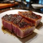 Two seared tuna steaks glistening with marinade, cut to show the pink center.