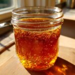 Close-up of a glass jar filled with golden pumpkin spice syrup on a wooden surface.