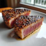 Two seared Tuna Steaks with a pepper crust on a white plate, showing the pink center.