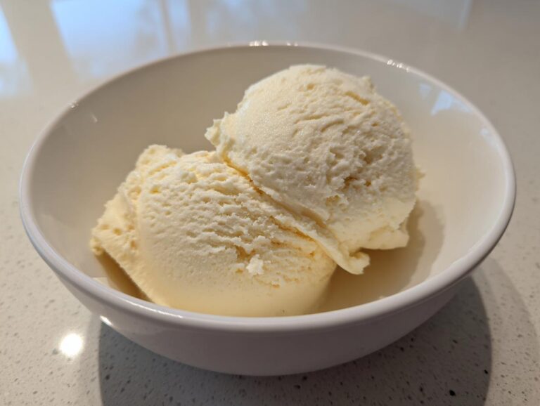 Two scoops of creamy cottage cheese ice cream in a white bowl on a countertop.