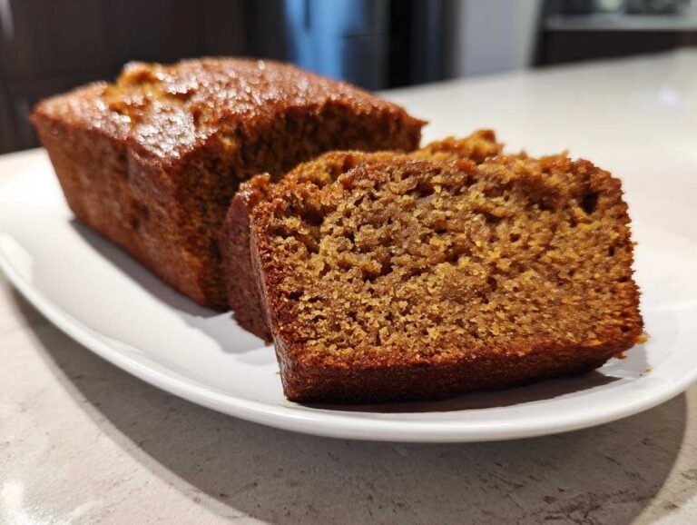 A loaf of keto pumpkin bread with a slice cut, displayed on a white plate.