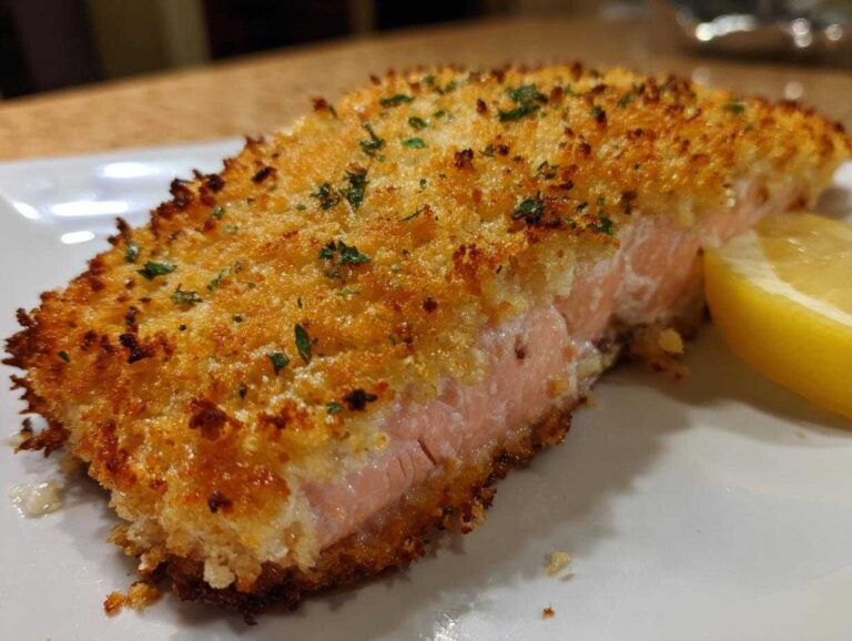 A close-up of parmesan crusted salmon on a white plate, garnished with parsley and a lemon wedge.