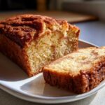 A loaf of snickerdoodle zucchini bread with a slice cut, showcasing the texture and cinnamon sugar topping.