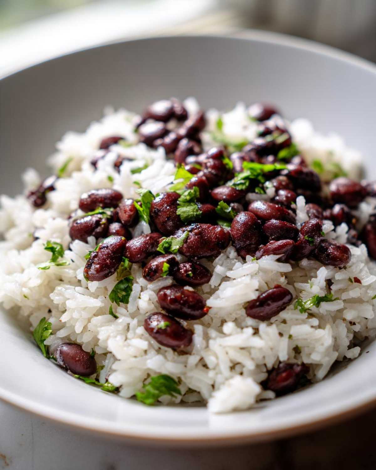 A close-up shot of fluffy white rice topped generously with seasoned black beans and fresh cilantro, showcasing the black beans and rice dish.