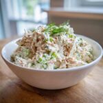 A generous serving of creamy crab salad mixed with celery and topped with fresh dill in a white bowl.