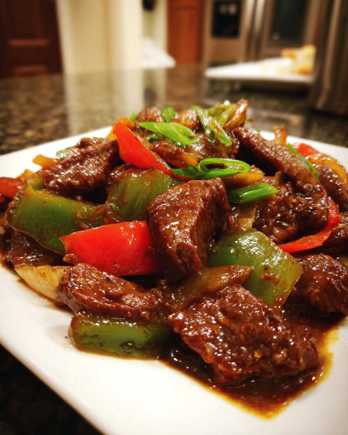 A close-up of saucy pepper steak featuring tender beef, green, and red bell peppers, garnished with scallions.