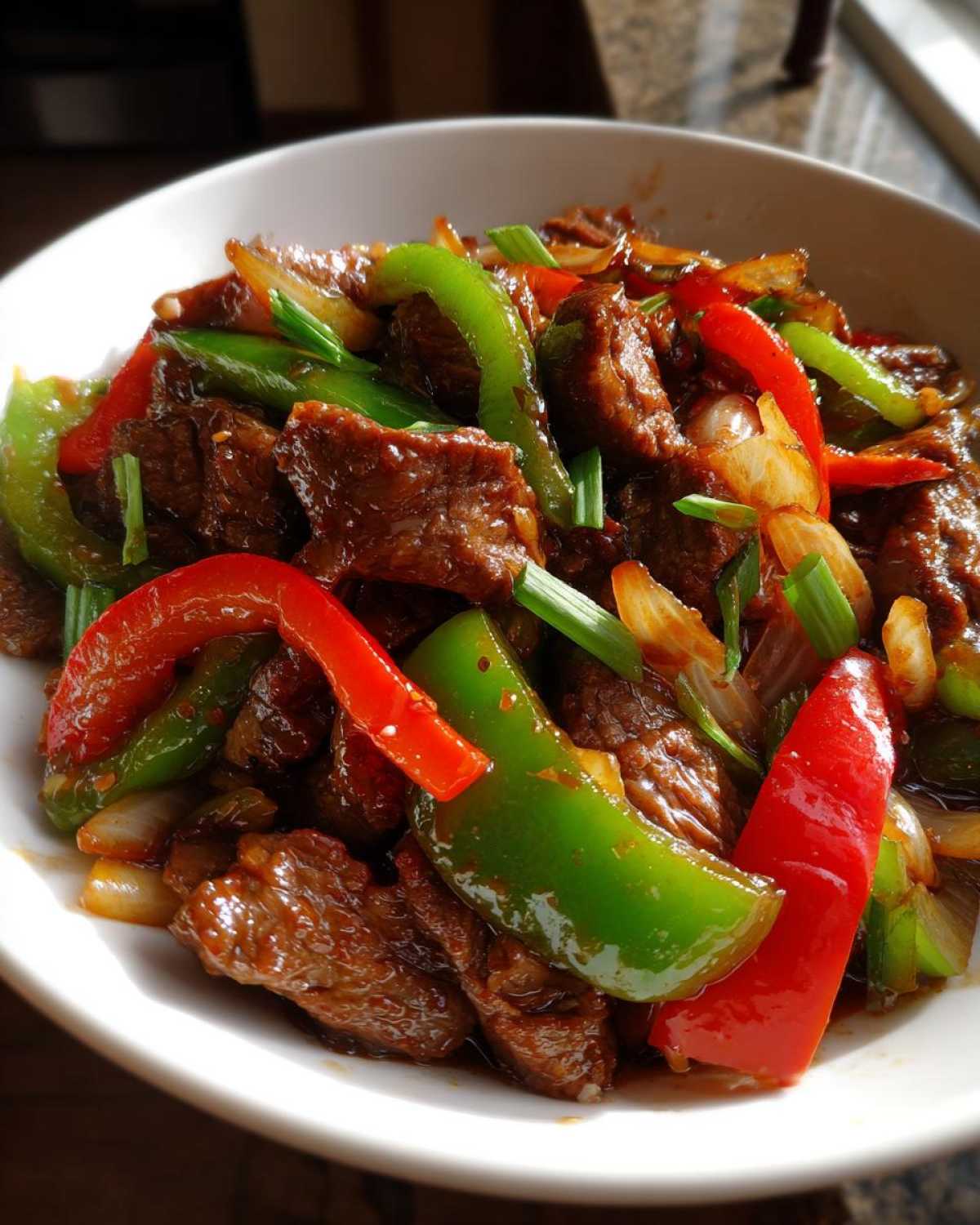 Close-up of savory pepper steak featuring tender beef, bright red and green bell peppers, and onions in a glossy sauce.