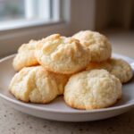 A close-up of several golden, slightly craggy butter cookie mounds piled on a light gray plate.