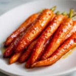 Close-up of perfectly glazed roasted carrots with slight charring, served on a white plate.
