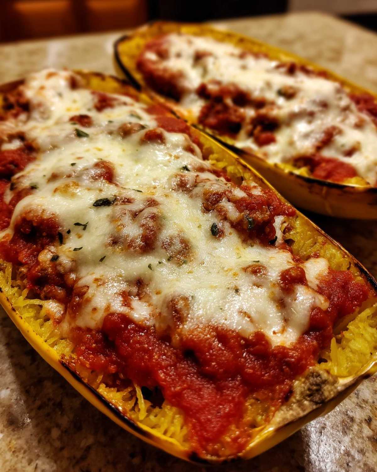 Two baked halves of spaghetti squash lasagna topped with melted mozzarella cheese and rich red sauce.