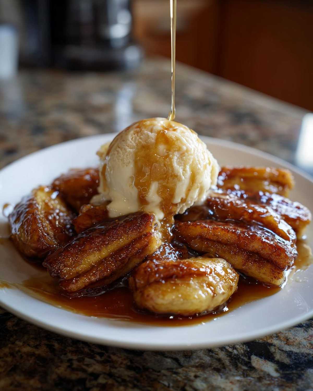 A scoop of vanilla ice cream topped with caramel sauce being drizzled over caramelized bananas foster on a white plate.