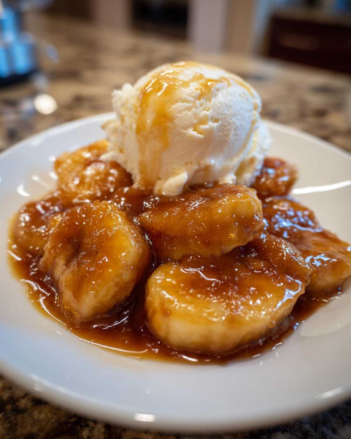 A serving of warm bananas foster topped with a scoop of vanilla ice cream drizzled with caramel sauce.