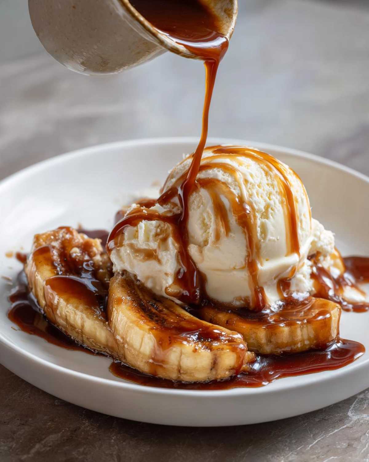 A scoop of vanilla ice cream sits atop caramelized bananas as rich sauce is poured over the Bananas Foster.