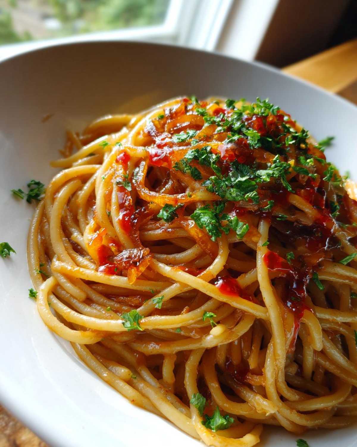 Close-up of a white bowl filled with caramelized onion pasta, topped with sweet onions and fresh parsley.
