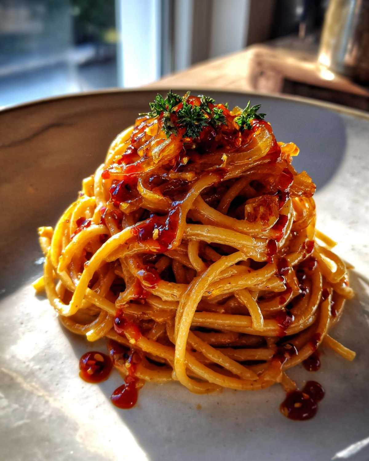 A tall swirl of spaghetti coated in sauce and caramelized onion pasta, topped with chili oil and parsley.