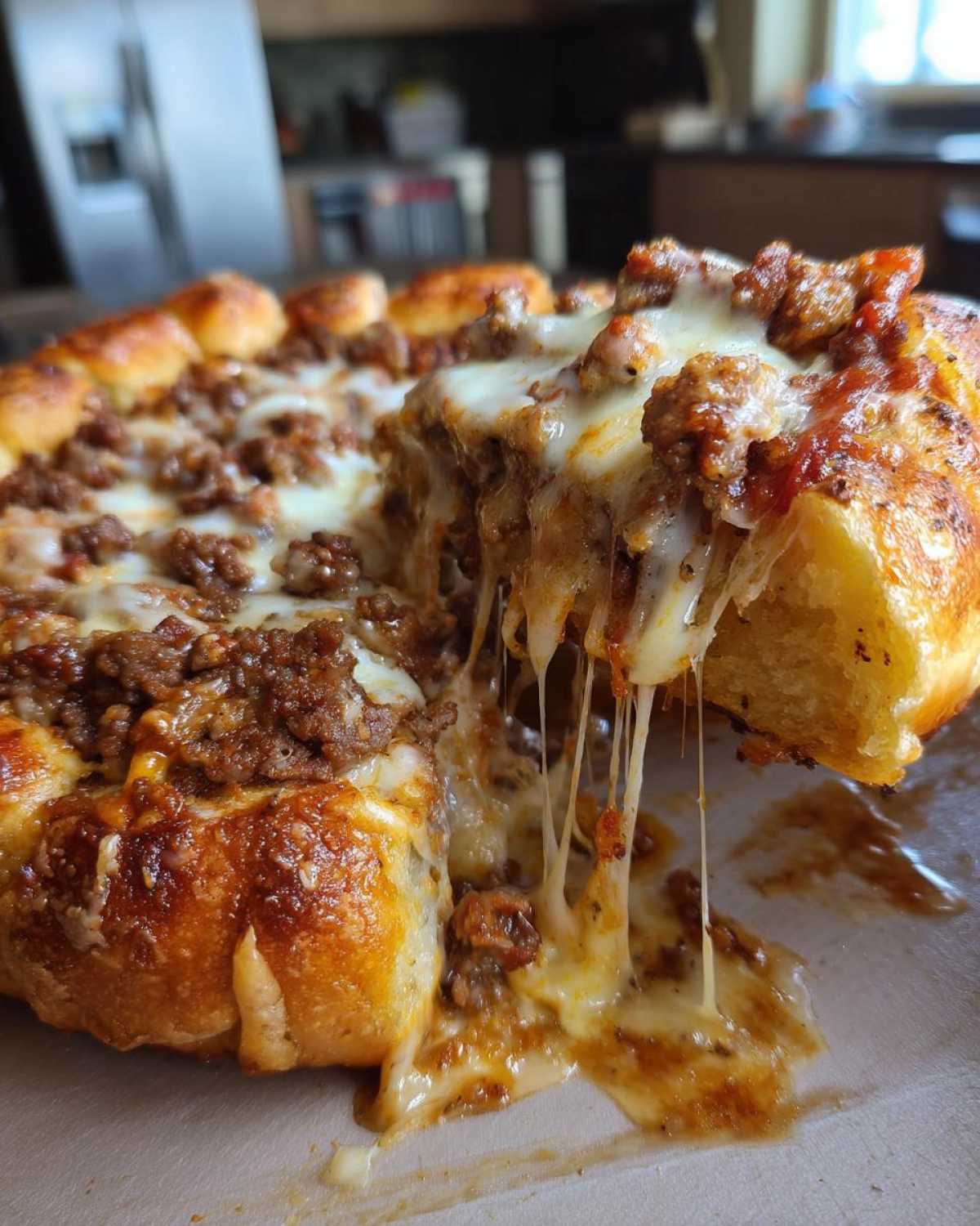 A slice of cheesy garbage bread being pulled away, showing long, gooey cheese strings and a savory meat topping.