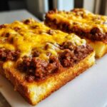 Close-up of two open-faced Texas Toast Sloppy Joes topped with saucy ground meat and melted cheddar cheese.