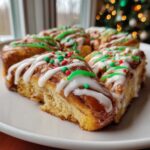 Close-up of freshly baked christmas tree cinnamon rolls topped with white icing, green drizzle, and holiday sprinkles.