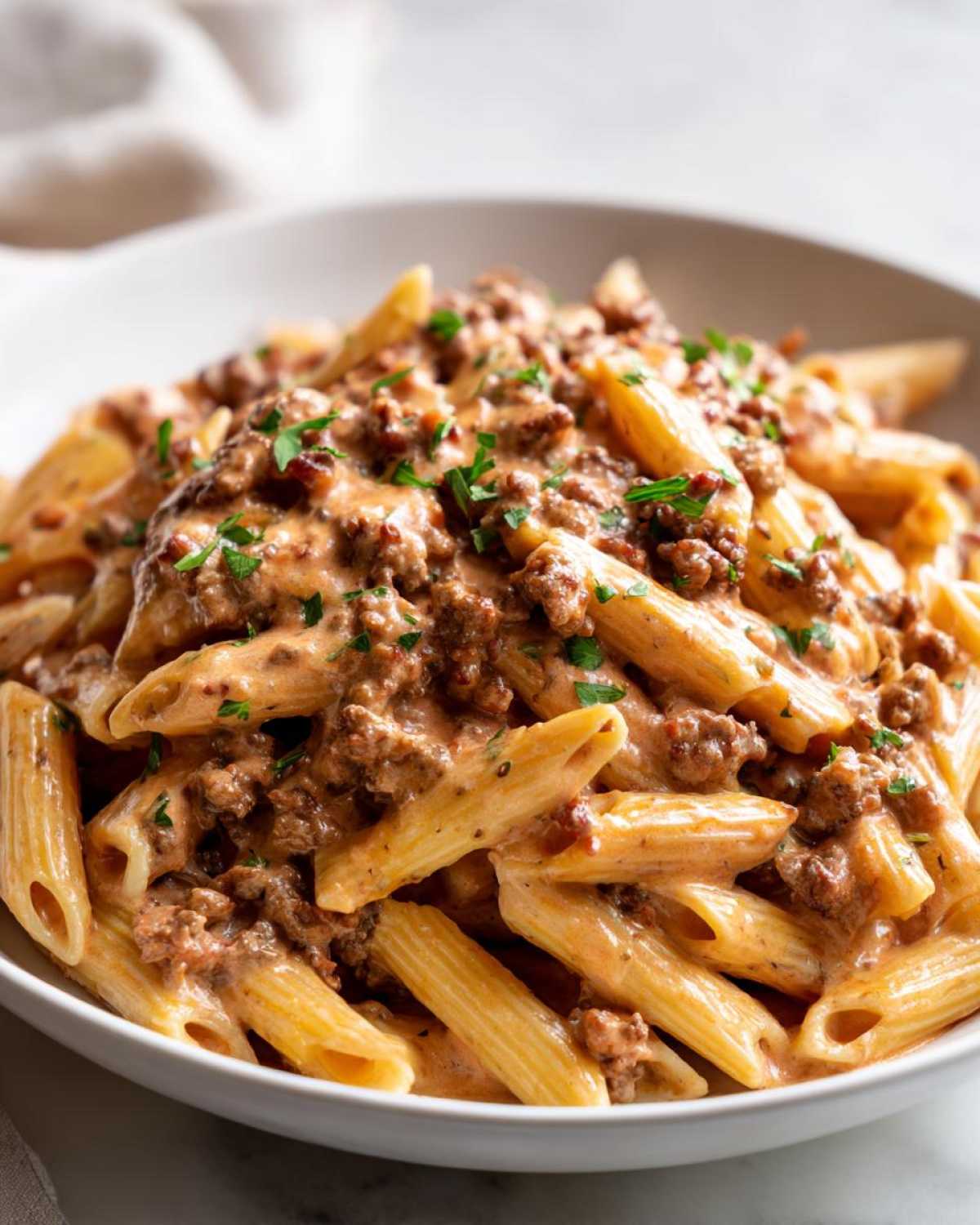 A close-up view of penne pasta coated in a rich, creamy beef sauce, garnished with fresh parsley, representing creamy beef pasta.