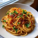 A close-up of creamy caramelized onion pasta topped with fresh parsley and red pepper flakes in a white bowl.