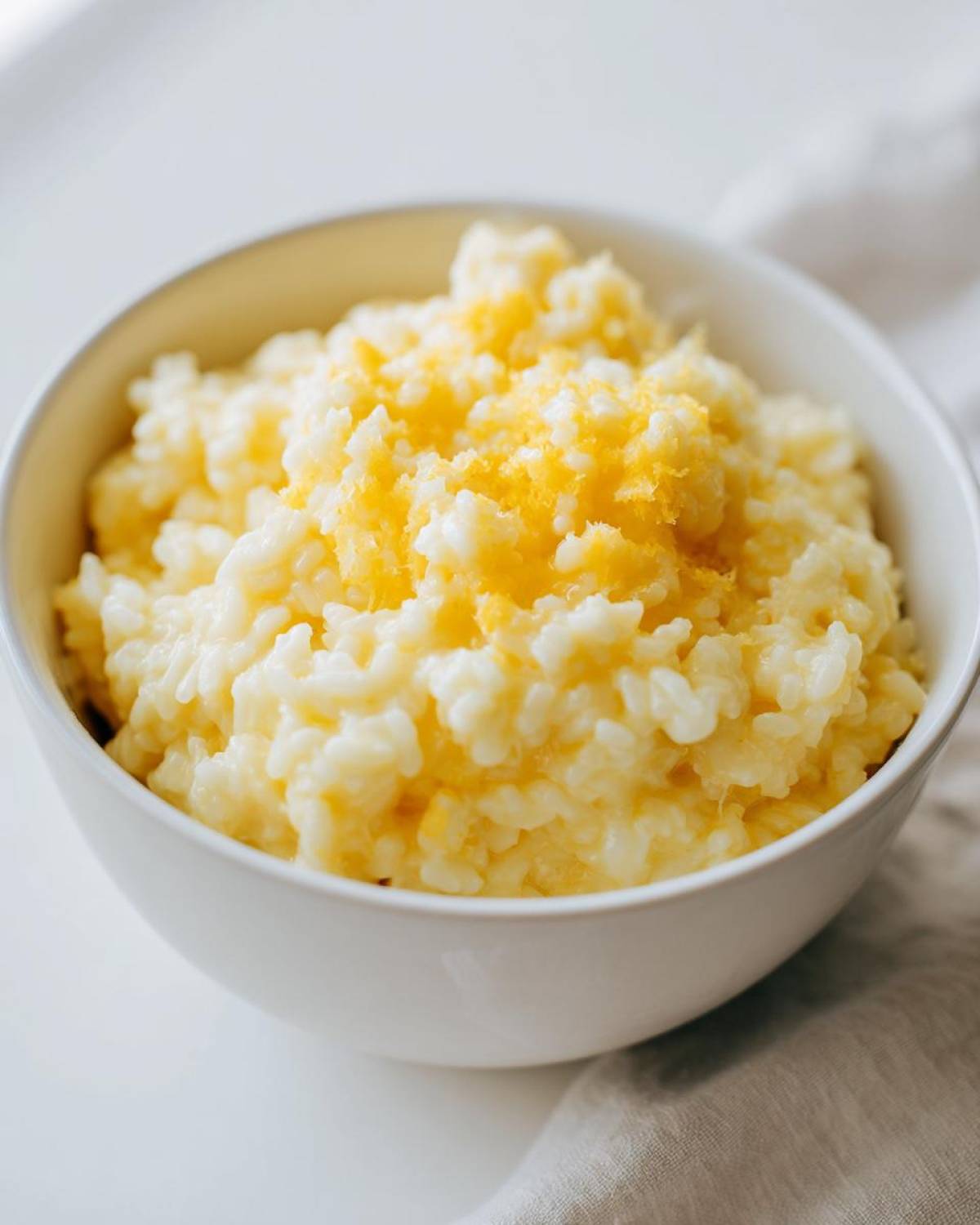 Close-up of creamy cheesy rice served in a white bowl, topped with bright yellow citrus zest.