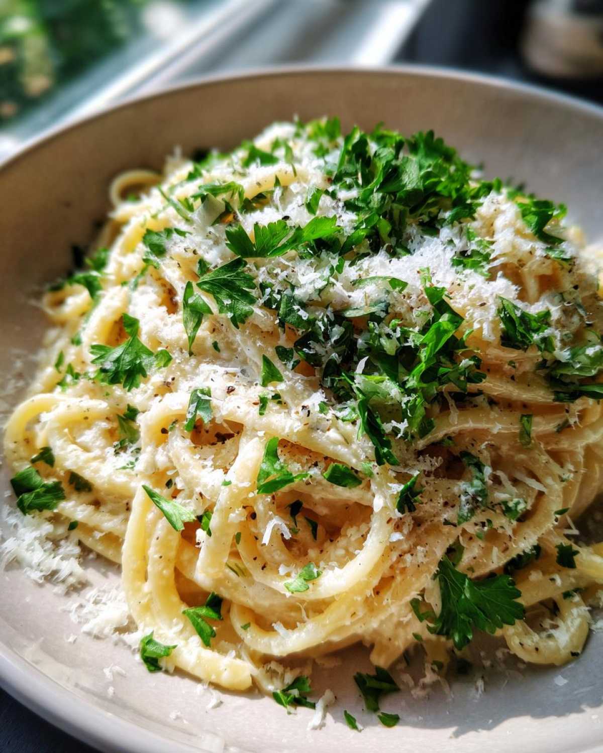 A close-up of creamy parmesan pasta tossed in sauce, generously topped with grated cheese and fresh parsley.
