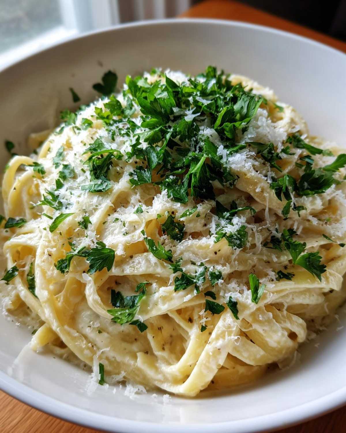 Close-up of creamy fettuccine parmesan pasta generously topped with grated cheese and fresh chopped parsley.