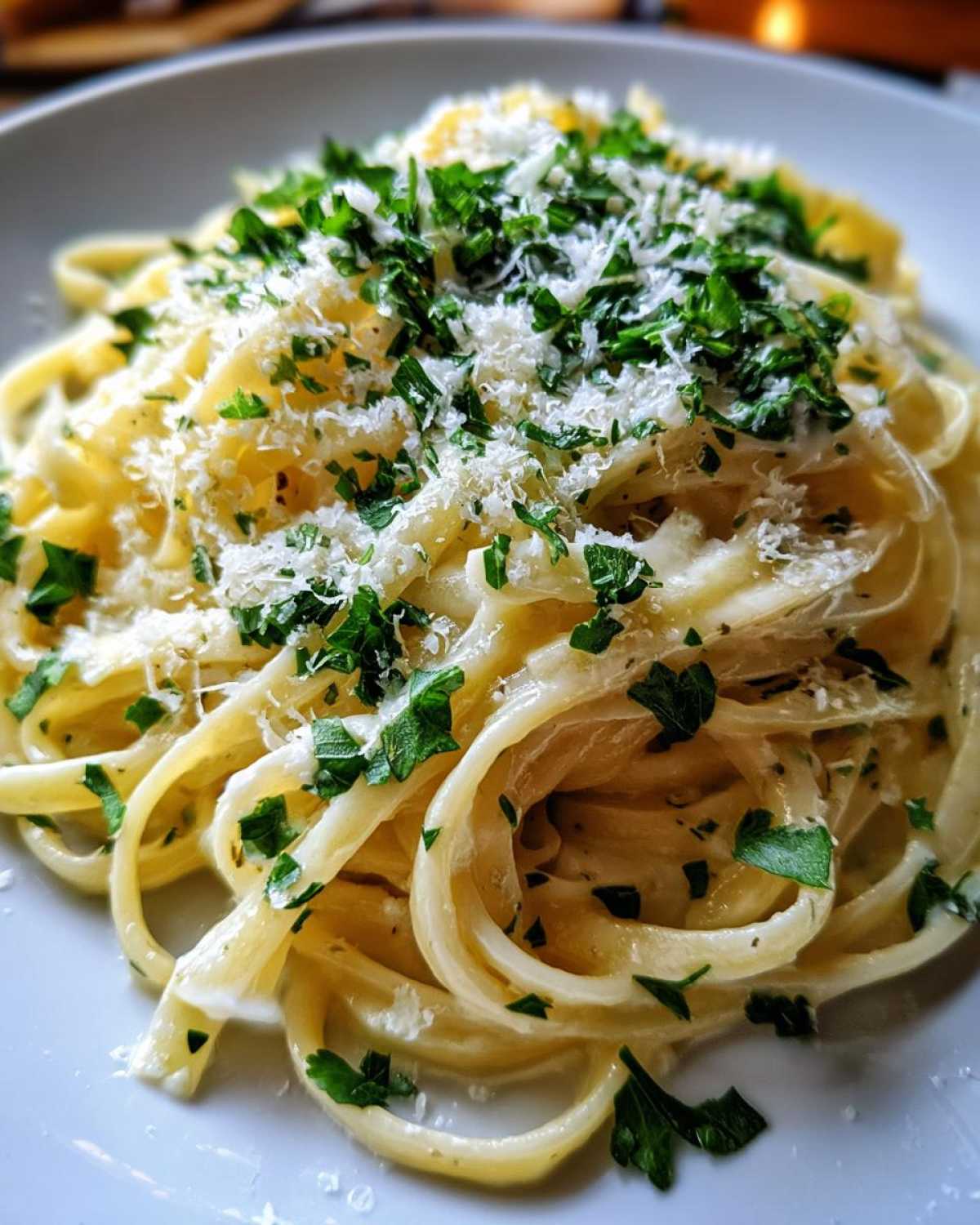 Close-up of creamy fettuccine tossed in sauce, topped with grated parmesan pasta and fresh chopped parsley.