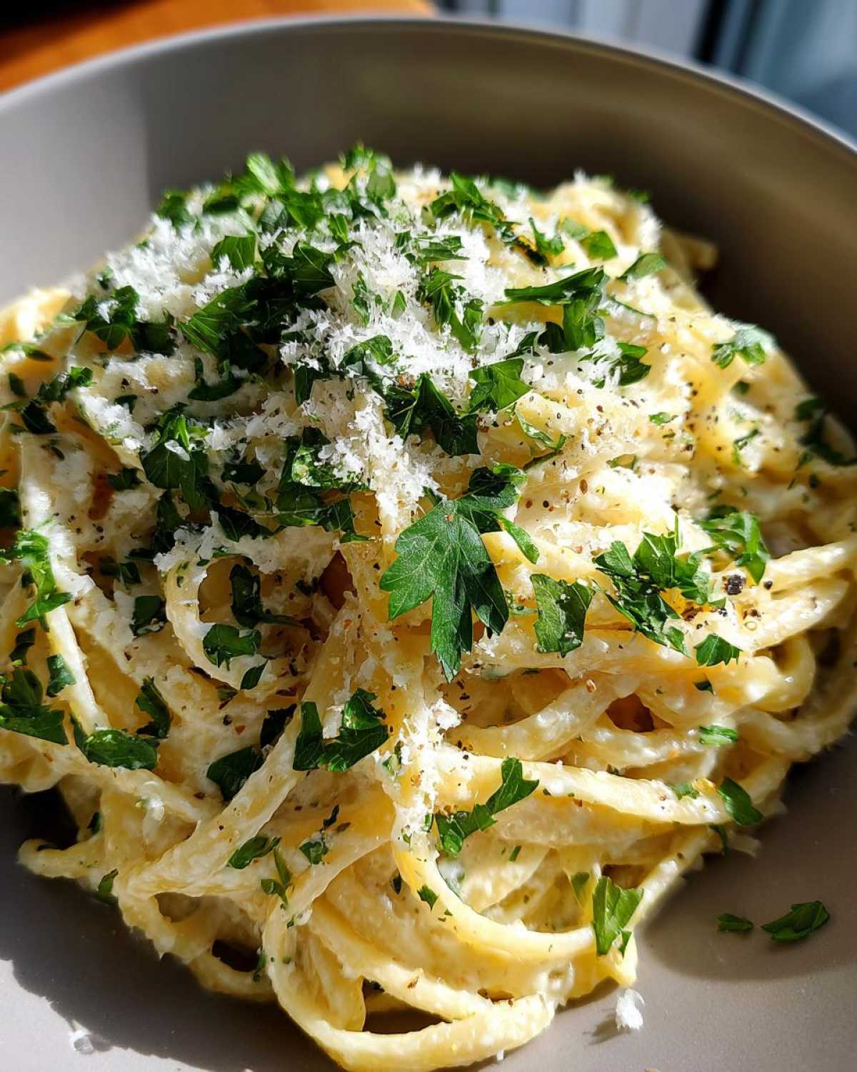 Close-up of creamy parmesan pasta tossed in sauce, generously topped with grated cheese and fresh parsley.
