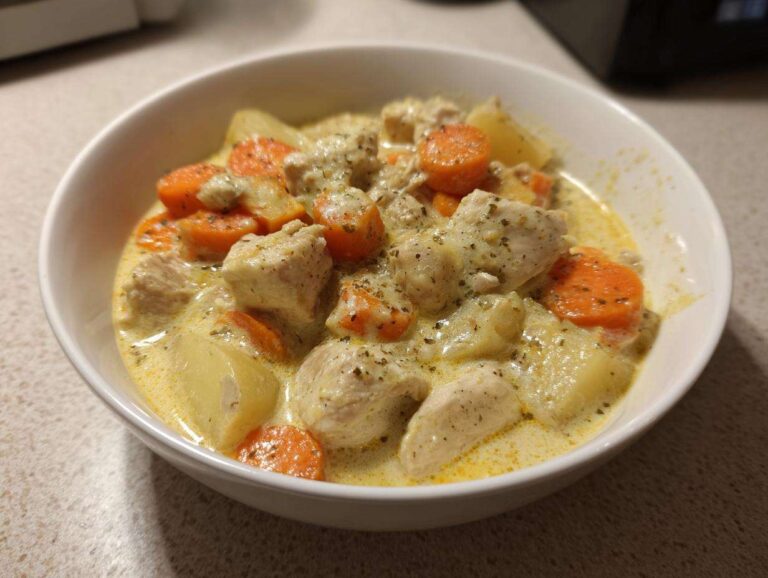 A close-up of a hearty slow cooker chicken stew featuring chunks of chicken, carrots, and potatoes in a creamy sauce.