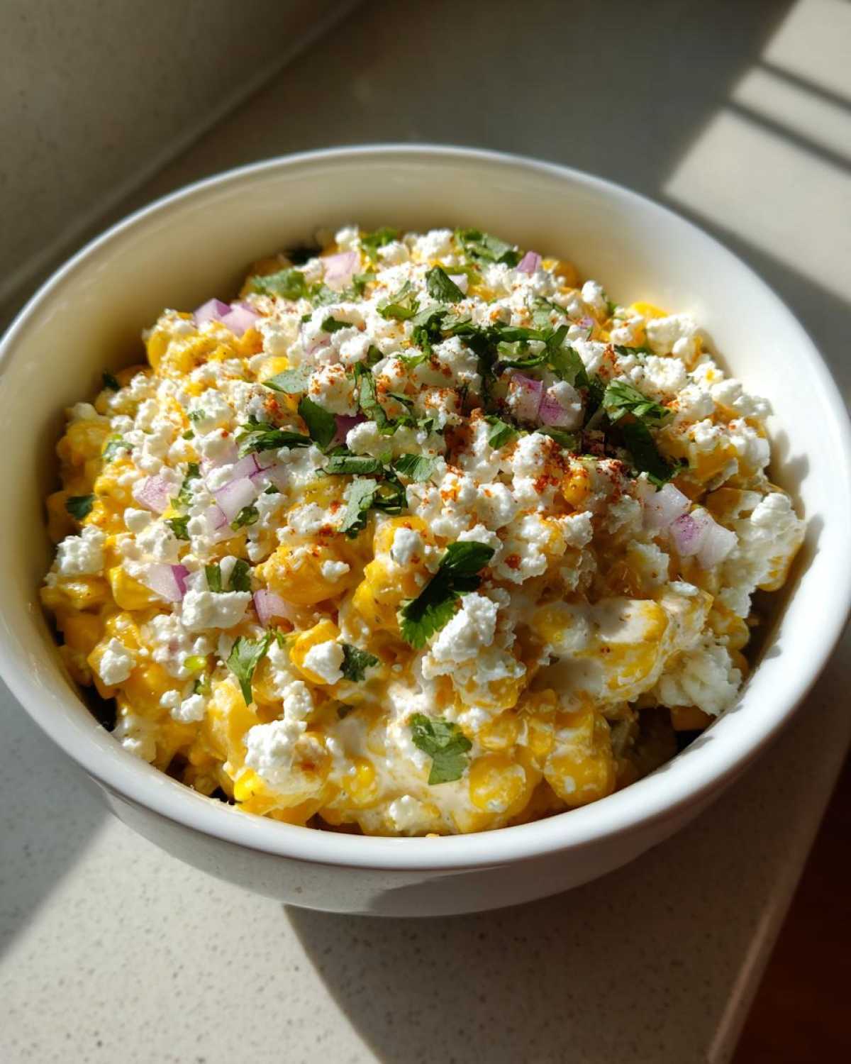 Close-up of a creamy street corn salad topped with cotija cheese, cilantro, red onion, and chili powder.