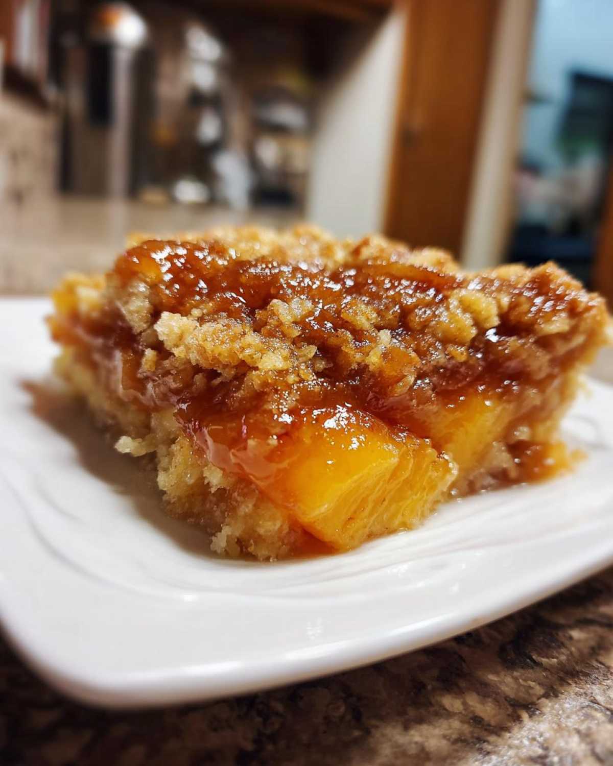 A close-up, appetizing slice of easy southern peach cobbler with a gooey topping on a white plate.