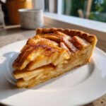A close-up slice of a delicious apple tart, featuring layered apples dusted with cinnamon, served on a white plate.