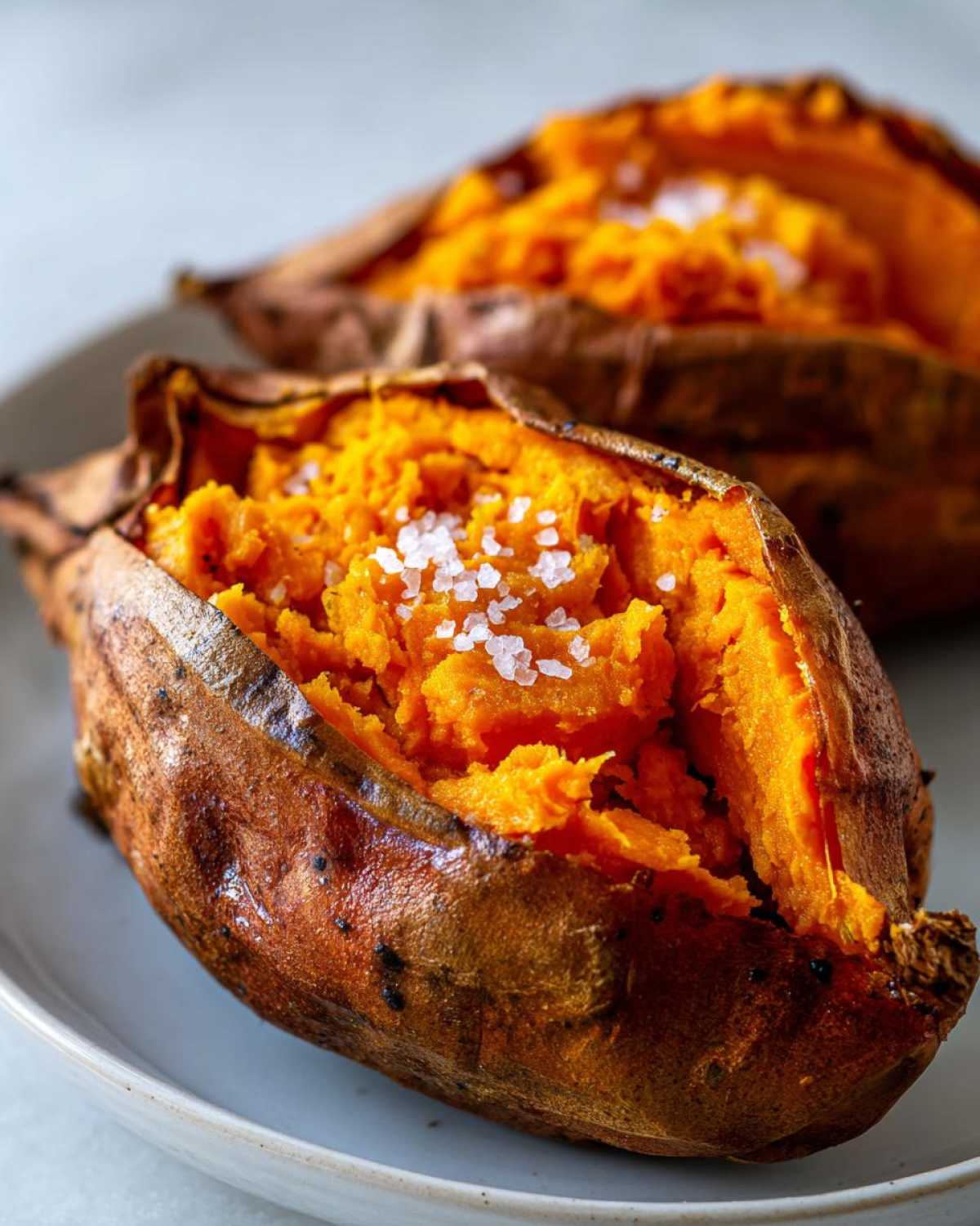 Close-up of a fluffy baked sweet potato, split open and topped with coarse sea salt flakes.