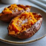 Close-up of a fluffy baked sweet potato, split open and topped with coarse sea salt.