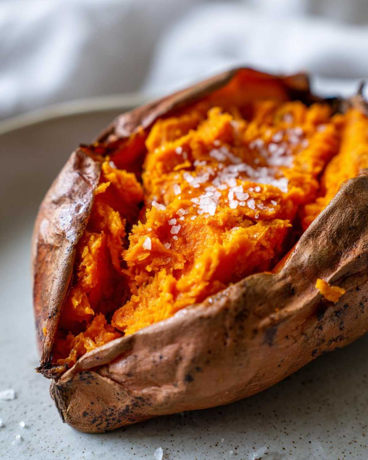 Close-up of a fluffy baked sweet potato, split open and topped with coarse sea salt.