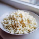 A close-up of fluffy, white cauliflower rice seasoned lightly with pepper, mounded on a small white plate.
