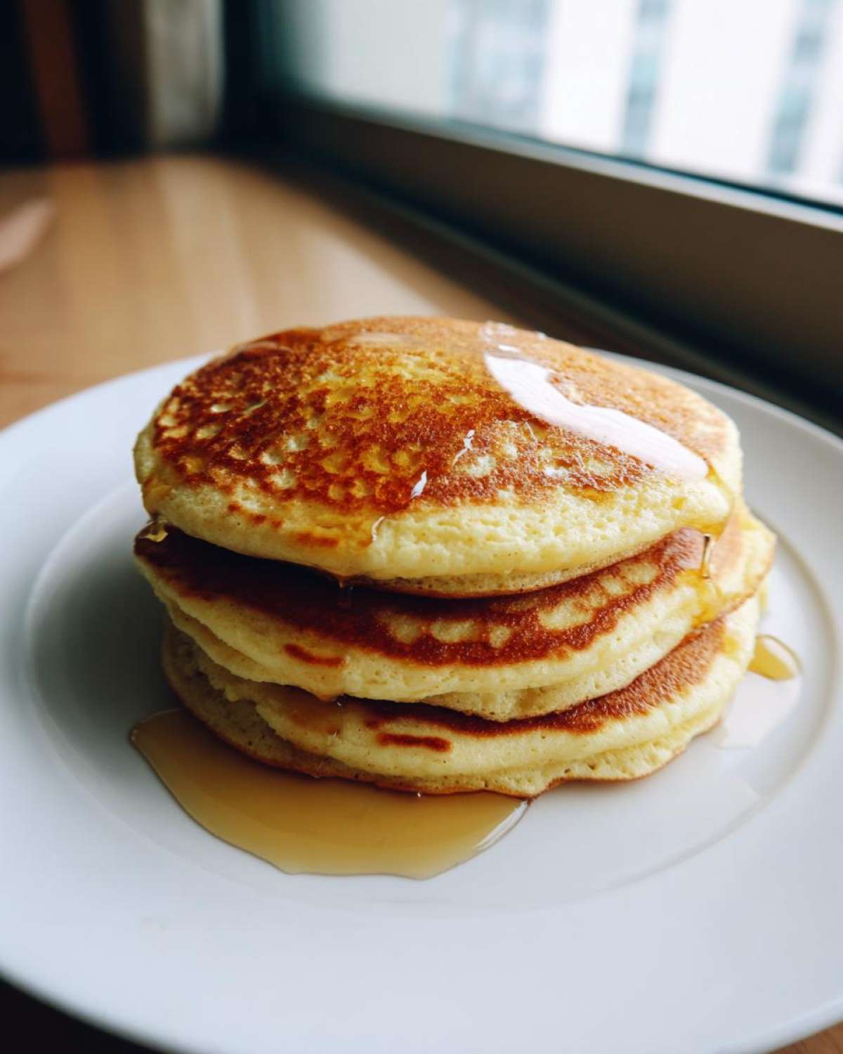 A stack of three fluffy coconut flour pancakes drizzled with maple syrup on a white plate.