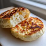 Close-up of homemade English muffins split open, showing the signature airy, hole-filled texture.