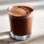 A tall glass filled with rich, dark frozen hot chocolate topped with cocoa powder.