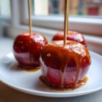 Close-up of a glossy caramel apple dripping with rich caramel sauce, served on a white plate.