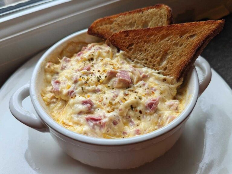 Close-up of hot reuben dip in a white ramekin, topped with spices and served with two toasted bread triangles for dipping.