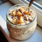 Close-up of apple cinnamon overnight oats in a glass jar, topped with diced apples and cinnamon.