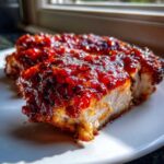 Close-up of a thick slice of juicy cranberry chicken breast covered in a thick, glistening red cranberry glaze.