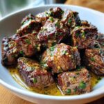 Close-up of tender, browned crockpot steak bites coated in a rich garlic butter sauce and fresh parsley.