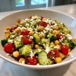 Close-up of a vibrant mediterranean chickpea salad with cucumbers, tomatoes, and feta cheese in a white bowl.