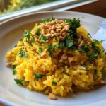 A serving of vibrant yellow mediterranean rice topped with chopped parsley and toasted pine nuts.