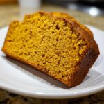 A thick slice of moist pumpkin bread showing its rich orange color and tender crumb texture.