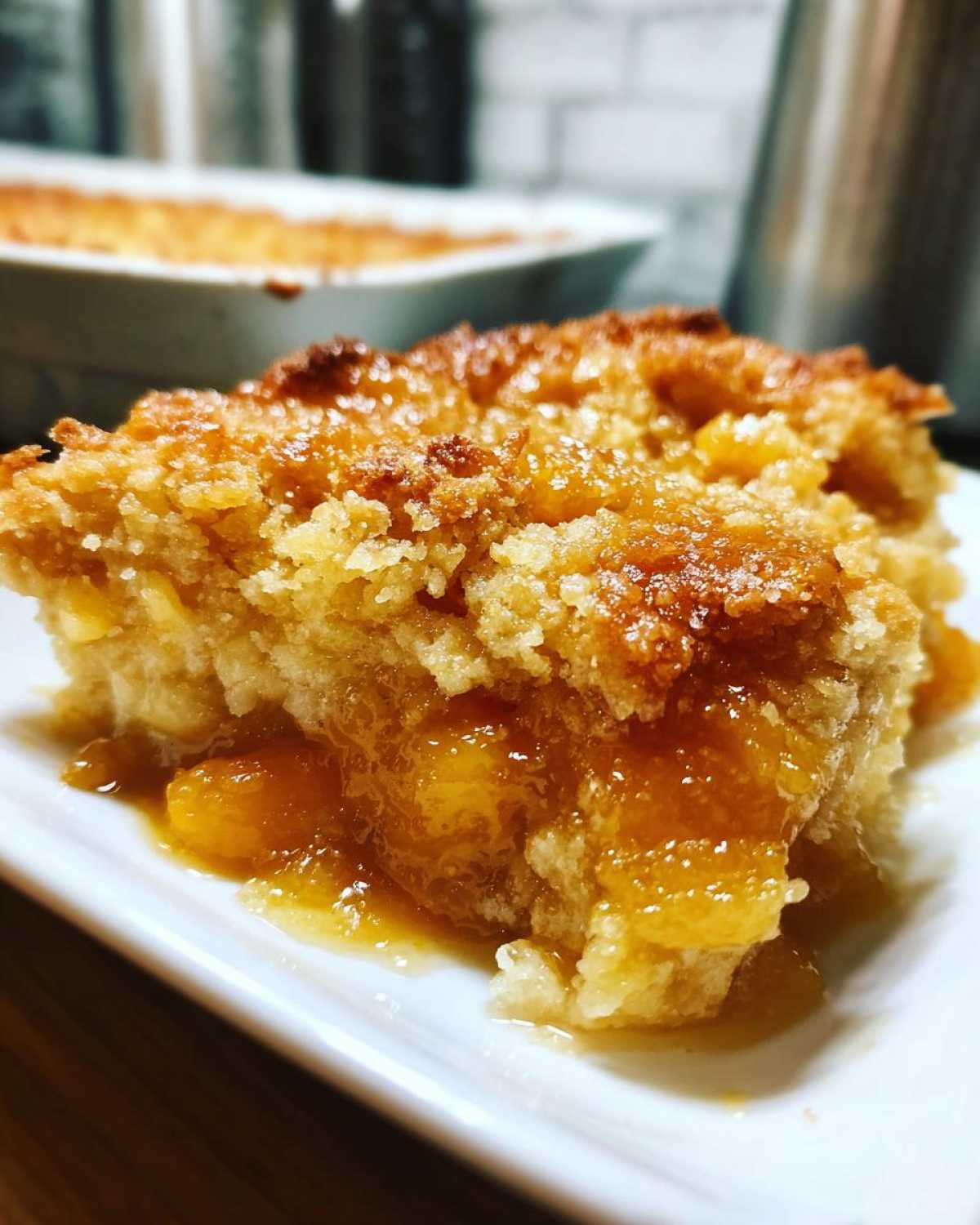 A close-up, decadent serving of southern peach cobbler with a sugary, browned topping and gooey peach filling.