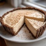 A creamy, light brown no bake eggnog pie with a dark crust, dusted with cinnamon, with one slice cut out.